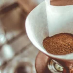 Close up of coffee being poured from a carafe into a mug near a drip brewer.