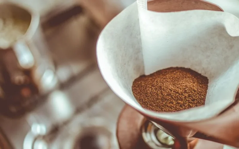 Close up of coffee being poured from a carafe into a mug near a drip brewer.