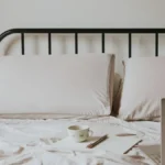A steaming cup of coffee resting on a nightstand near a bed in a soft lit room.
