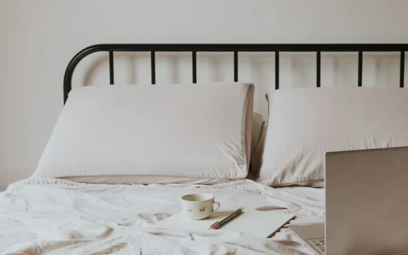 A steaming cup of coffee resting on a nightstand near a bed in a soft lit room.