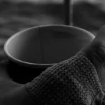 A person holding a warm coffee mug on a rustic wooden table near tactile textures.