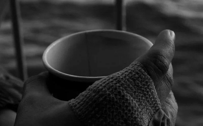 A person holding a warm coffee mug on a rustic wooden table near tactile textures.