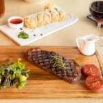 A glass of red Bordeaux wine and a bottle on a dark wooden table.