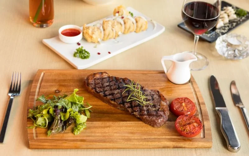 A glass of red Bordeaux wine and a bottle on a dark wooden table.