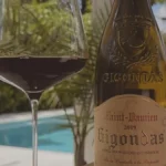A glass of red wine on a wooden table overlooking a sunny Southern Rhône vineyard.