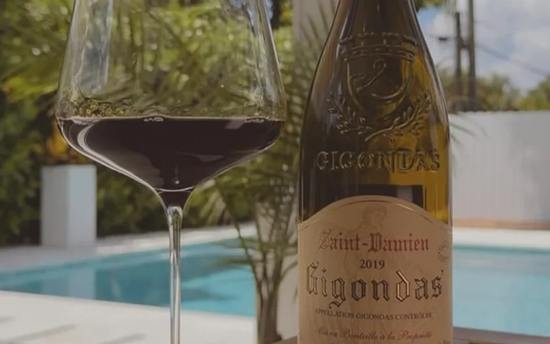 A glass of red wine on a wooden table overlooking a sunny Southern Rhône vineyard.