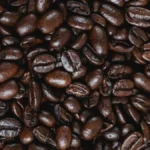 Light roast coffee beans spilling from an open bag on a dark wood table.