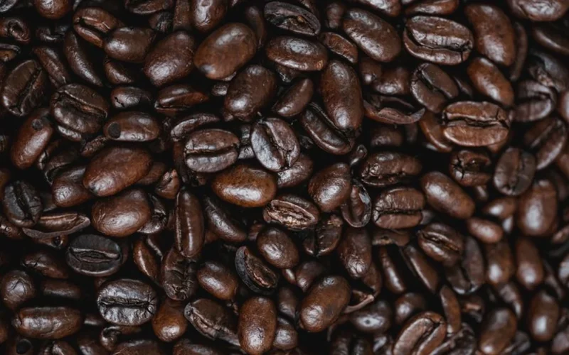 Light roast coffee beans spilling from an open bag on a dark wood table.