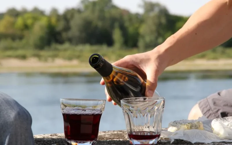 Red wine being poured into a glass on a dark wooden surface.