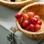 A traditional bamboo Zaranda de Coligüe and red grapes on a rustic wooden table.