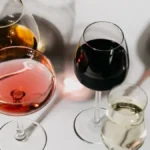 Three glasses of red wine with different hues sitting on a dark slate tabletop.