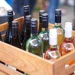 Twelve bottles of Central Otago Pinot Noir arranged in a wooden crate overlooking a vineyard.