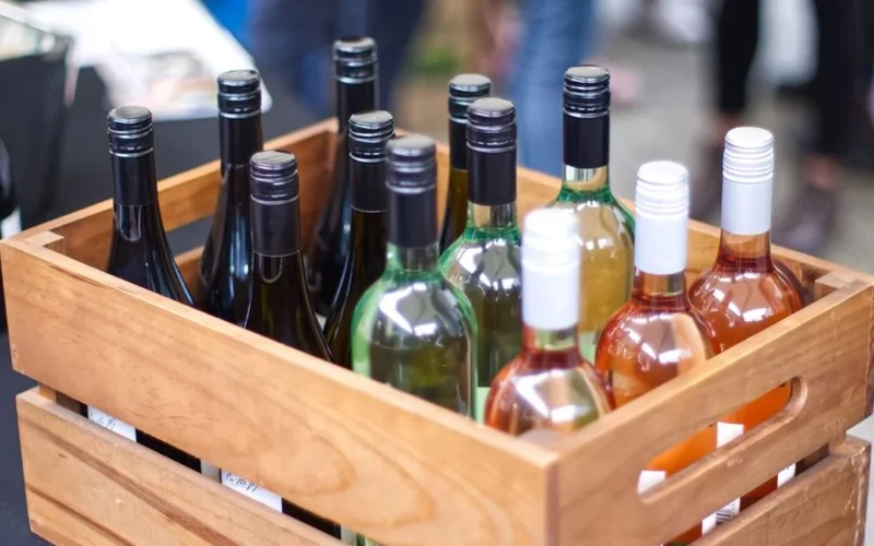 Twelve bottles of Central Otago Pinot Noir arranged in a wooden crate overlooking a vineyard.