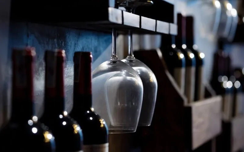A glass of deep red Bordeaux wine on a rustic wooden surface in dim lighting.