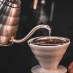 Close up of water being poured from a kettle into a glass pour over coffee maker.