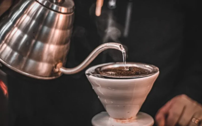 Close up of water being poured from a kettle into a glass pour over coffee maker.