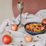 A glass of red wine next to dried raspberries and plums on a stone surface.