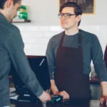A friendly barista serving a warm cup of coffee to a smiling customer in a cafe.