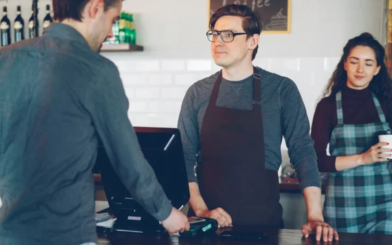 A friendly barista serving a warm cup of coffee to a smiling customer in a cafe.