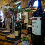 Four different wine bottles and two glasses resting on a dark wooden table in a restaurant.