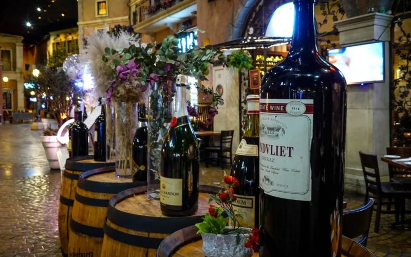 Four different wine bottles and two glasses resting on a dark wooden table in a restaurant.