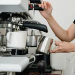 Barista preparing a specialty coffee drink with syrups and milk in a busy cafe.