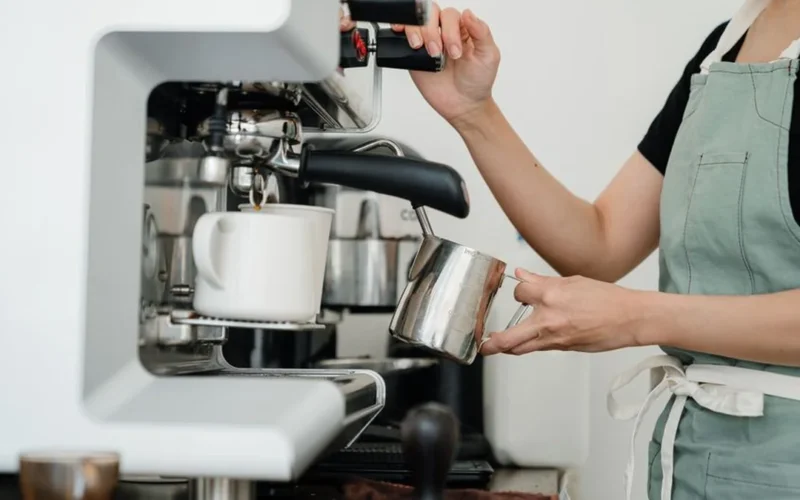 Barista preparing a specialty coffee drink with syrups and milk in a busy cafe.