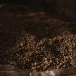 Large burlap sacks filled with raw green coffee beans in an industrial warehouse.