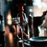 A dark wine bottle and a glass of red wine on a wooden restaurant table.