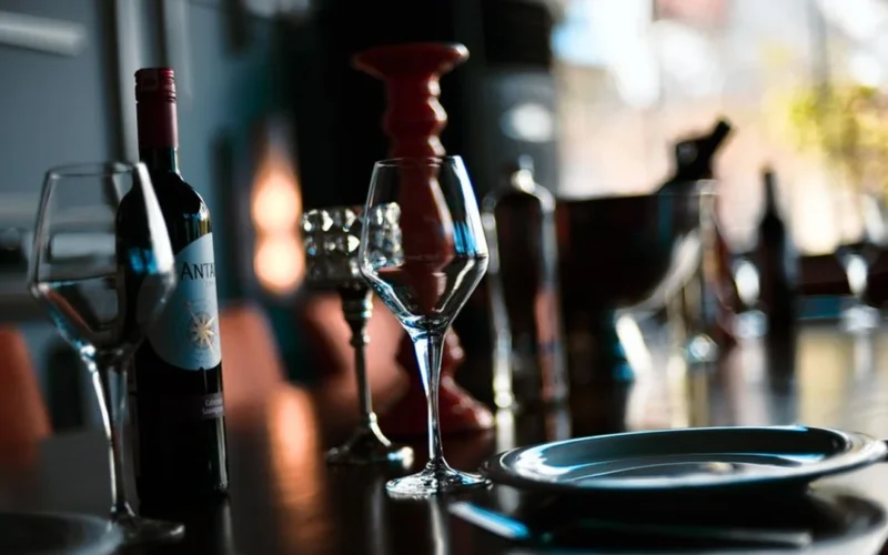 A dark wine bottle and a glass of red wine on a wooden restaurant table.