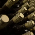 Wine bottles in a wooden crate positioned in a sunny vineyard during a heatwave.