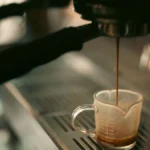 Close-up of espresso pouring from a professional portafilter into a glass cup on a dark countertop.