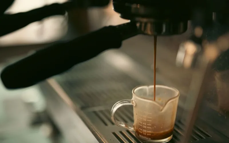 Close-up of espresso pouring from a professional portafilter into a glass cup on a dark countertop.