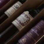 Deep red wine pouring from a cardboard box spout into a glass on wood.