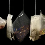 A green soda bottle and black tea bags on a marble table with ice cubes.