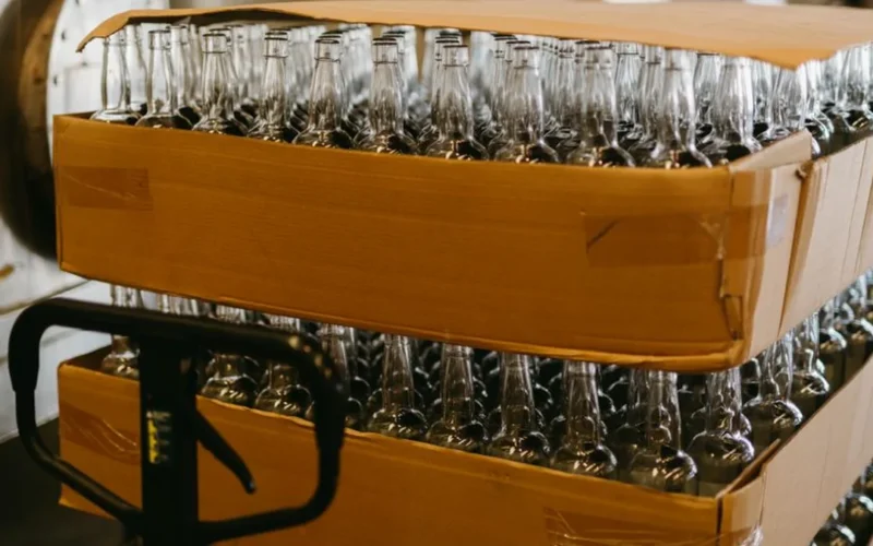 A bottle of red wine resting on a wooden pallet inside a large warehouse setting.
