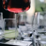 A glass of red wine sits on a table next to various canned beverages.