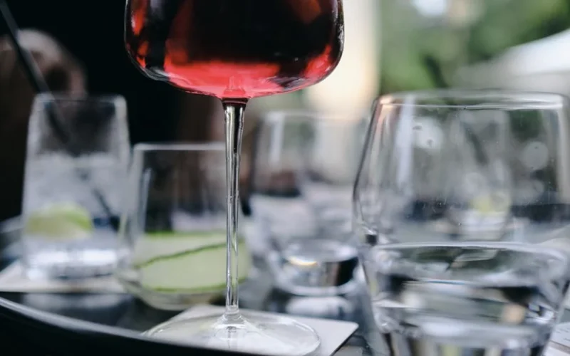 A glass of red wine sits on a table next to various canned beverages.