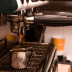 Close up of fresh espresso being poured into a white ceramic cup at a coffee festival.