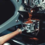 Close-up of a professional Macap coffee grinder dispensing grounds into a portafilter in a busy cafe.