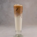 A tall glass of iced coffee with layers of milk, foam, and syrup.