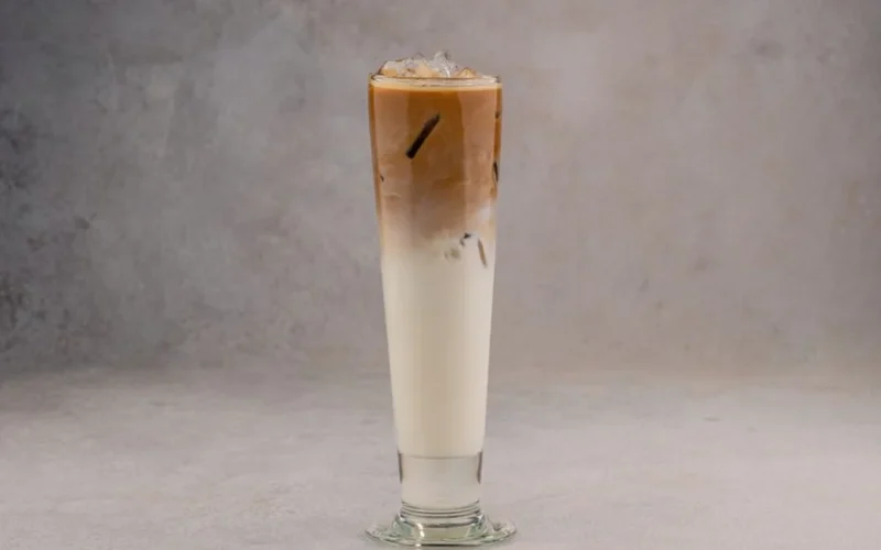 A tall glass of iced coffee with layers of milk, foam, and syrup.