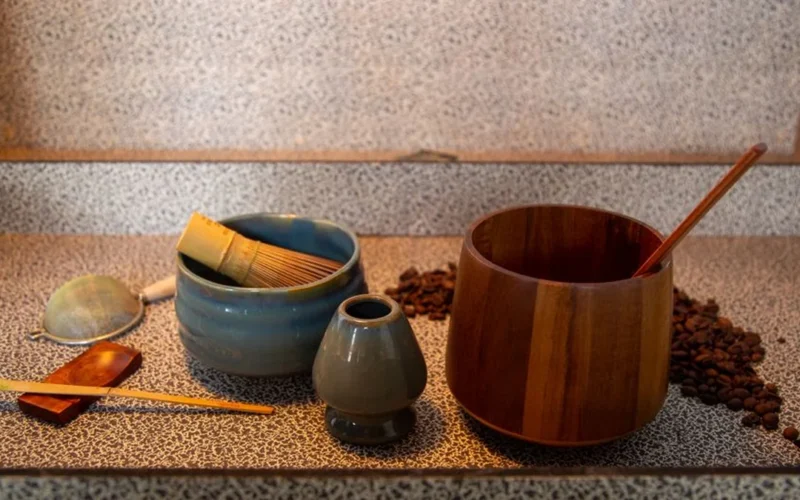 Bamboo whisk stirring vibrant green ceremonial grade matcha in a ceramic bowl on marble.