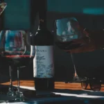 An elegant slim glass bottle of red wine and a filled glass on stone.