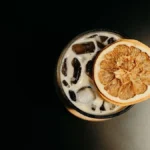 A coffee cocktail with a large ice sphere next to a book and Greek sculpture.