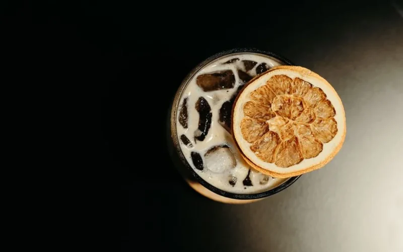 A coffee cocktail with a large ice sphere next to a book and Greek sculpture.