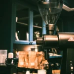 A black MiiCoffee DF54 coffee grinder on a dark granite kitchen counter with coffee grounds.