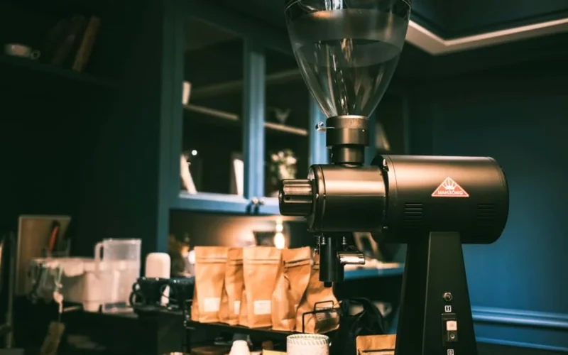 A black MiiCoffee DF54 coffee grinder on a dark granite kitchen counter with coffee grounds.