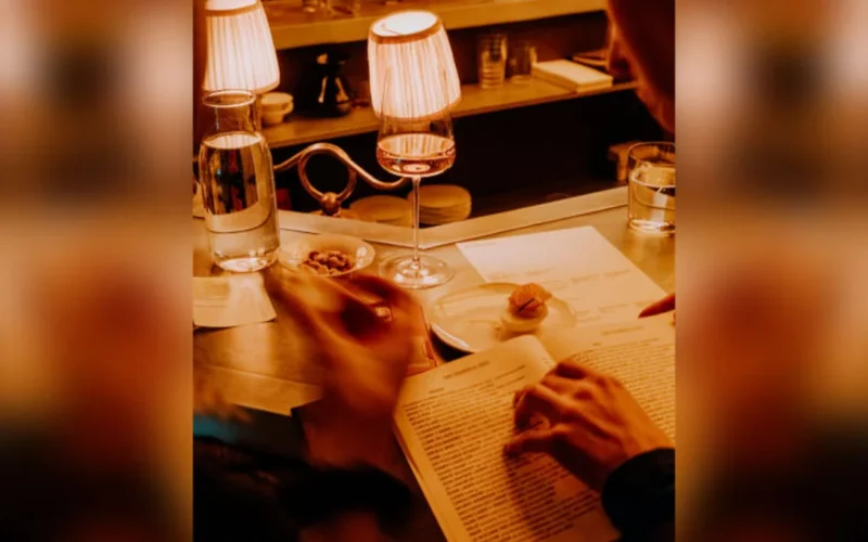 A printed wine list and a glass of red wine on a restaurant table.