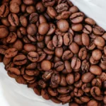 Dark roasted coffee beans scattered next to a black coffee bag on a dark surface.
